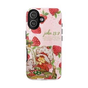May include: A pink phone case featuring a strawberry pattern and the text "john 13:7". The case has a cartoon illustration of a character in a bed with a white cat. The case is designed to fit a smartphone.