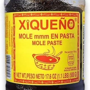 Puede incluir: Un frasco de plástico transparente lleno de pasta de mole color marrón oscuro, con una tapa amarilla de rosca. La etiqueta amarilla muestra la marca Xiqueño, el texto Mole mmm en pasta y un peso neto de 500 gramos.