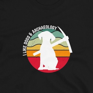 May include: Black t-shirt featuring a retro-style graphic of a dog holding a pickaxe. The graphic reads "I Like Dogs & Archaeology".