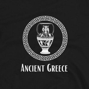 Puede incluir: Camiseta negra con un diseño blanco de un jarrón griego antiguo dentro de un borde circular con un diseño de clave griega. Las palabras "ANCIENT GREECE" están impresas debajo. La camiseta es de material suave.