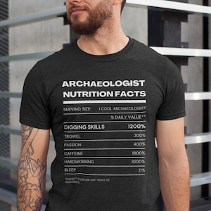 Peut inclure: Un t-shirt gris foncé chiné avec un graphique blanc qui indique "Archaeologist Nutrition Facts" et liste la valeur quotidienne en pourcentage des compétences de fouille, y compris la truelle, la passion, la caféine, le travail acharné et le sommeil. Le graphique est dans le style d'une étiquette de valeur nutritionnelle.