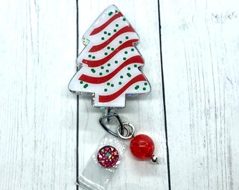 Op de afbeelding: Een kerstboomvormige badge reel met een witte achtergrond, rode strepen en groene stippen. De badge reel heeft een doorzichtige plastic band, een rode edelsteen en een rode kraal met een zilveren accent.