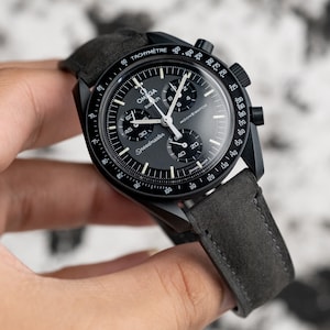 Peut inclure: Une montre chronographe Omega Speedmaster noire avec un bracelet en cuir noir. Le cadran de la montre comporte une échelle tachymétrique, un guichet date et une fonction chronographe. La montre est un design classique avec une touche sportive.