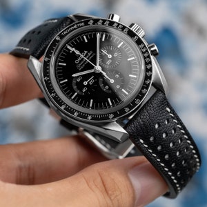 May include: A black chronograph wristwatch with a silver bezel and white markings. The watch has a black leather strap with white stitching and a perforated pattern.