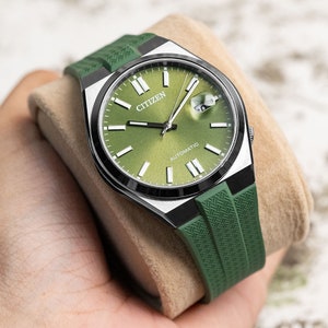 Puede incluir: Un reloj autom&aacute;tico Citizen con esfera verde, bisel negro y correa de caucho verde. La esfera del reloj tiene marcadores de hora en n&uacute;meros romanos blancos y una ventana de fecha en la posici&oacute;n de las 3 en punto.