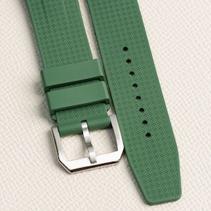 Puede incluir: Una correa de reloj de caucho verde con una hebilla plateada. La correa tiene un patr&oacute;n texturizado.