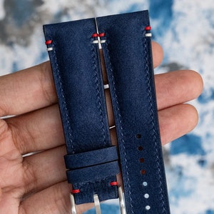 May include: A pair of dark blue watch straps with red stitching. The straps are made of a textured leather material.