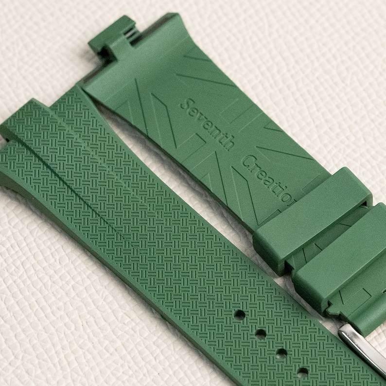 Puede incluir: Una correa de reloj verde con un patr&oacute;n tejido y el texto "Seventh Creation" grabado en la correa.