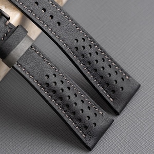 May include: Two black leather watch straps with white stitching and a perforated design.