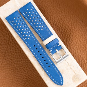 May include: A blue leather watch strap with white stitching and a perforated design. The strap has a silver buckle.