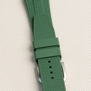 Puede incluir: Una correa de reloj de goma verde con un patr&oacute;n texturizado y una hebilla plateada.