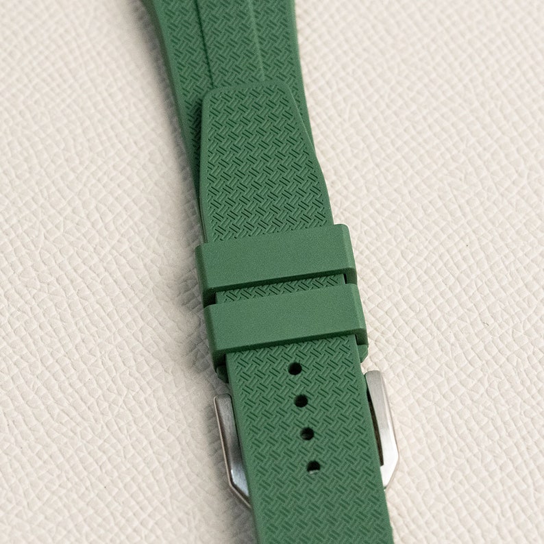Puede incluir: Una correa de reloj de goma verde con un patr&oacute;n texturizado y una hebilla plateada.