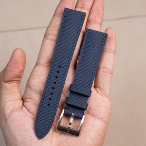 May include: Two dark blue watch straps with a textured finish. The strap on the left has a pointed end, while the strap on the right has a buckle.