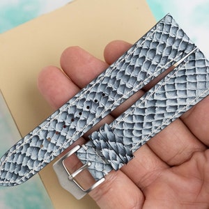 May include: A gray leather watch strap with a white stitched pattern. The strap has a silver buckle.