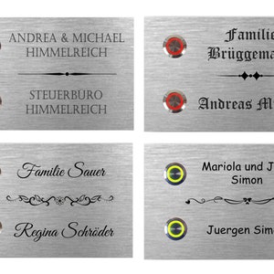 Op de afbeelding: Vier zilveren deurbelletjes met verschillende namen en knoppen. De deurbel linksboven heeft blauwe knoppen en zegt "Andrea & Michael Himmelreich" en "Steuerbüro Himmelreich". De deurbel rechtsboven heeft rode knoppen en zegt "Familie Brüggemann" en "Andreas Müller". De deurbel linksonder heeft groene knoppen en zegt "Familie Sauer" en "Regina Schröder". De deurbel rechtsonder heeft gele knoppen en zegt "Mariola und Jens Simon" en "Juergen Simon".