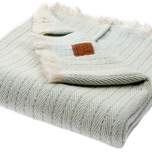 May include: A light blue and white herringbone throw blanket with a brown leather tag that says "GOLD CASE" and "HANDCRAFTED IN INDIA".