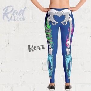 Pode incluir: Leggings azuis com um design de esqueleto com detalhes em verde e rosa. O esqueleto est&aacute; parcialmente quebrado e tem bandagens na perna.
