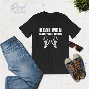 May include: Black t-shirt with white text that reads "Real Men Marry Rad Tech's" and two white skeleton hands making the "OK" sign.