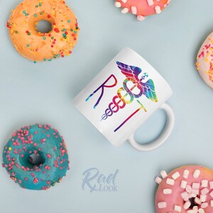 May include: White ceramic mug with a rainbow tie-dye design of a medical caduceus and the letters "R.N.T."  The mug is surrounded by colorful donuts.
