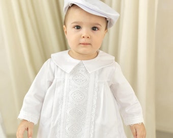 May include: A white christening gown with lace detailing and a white satin hat. The gown has a Peter Pan collar and long sleeves.
