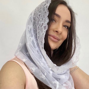 Puede incluir: Cobertura de cabeza de encaje blanco con un delicado patrón floral. El encaje es suave y transparente, y la cobertura de cabeza está diseñada para usarse sobre el cabello.