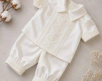 May include: A cream-colored short-sleeve shirt and matching pants set. The shirt features a pointed collar and a central vertical panel of intricate floral lace. The sleeves and the cuffs of the pants are finished with matching lace trim.