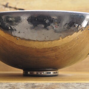 K&ouml;nnte beinhalten: Handgefertigte Keramikschale mit metallisch silberner und goldener Oberfl&auml;che. Die Schale hat eine breite, flache Form und steht auf einem kleinen, kreisf&ouml;rmigen Sockel. Das Innere reflektiert das Licht und erzeugt einen einzigartigen visuellen Effekt.