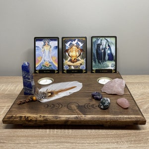 May include: A wooden altar with three tarot cards, two candles, a feather, and several crystals. The cards are "XIX Love", "XIV Self", and "X Wheel of Fortune".