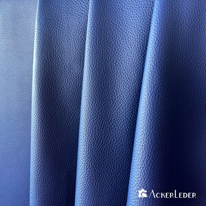 Può includere: Primo piano di un tessuto in pelle blu scuro con una superficie testurizzata. Il tessuto è piegato in tre sezioni, creando un motivo ondulato. Il tessuto è una pelle di alta qualità, perfetta per la tappezzeria o altri progetti di artigianato.