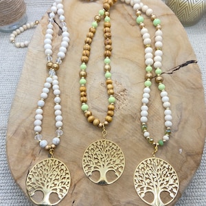 May include: Three necklaces with gold tree of life pendants. The necklaces are made with white, light green, and brown wooden beads.