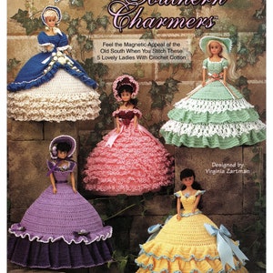 Puede incluir: Cinco muñecas de crochet vestidas con vestidos de estilo vintage. Las muñecas llevan vestidos en tonos de azul, verde, rosa, morado y amarillo. Todas las muñecas llevan sombreros y tienen el pelo largo y suelto. Las muñecas están todas de pie sobre un fondo de pared de ladrillo. El texto "Southern Charmers" está en la parte superior de la imagen.