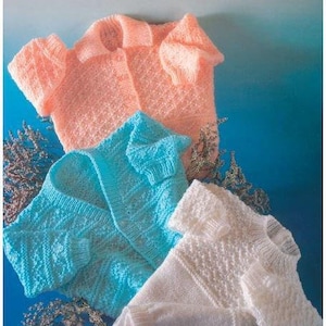 Puede incluir: Tres cárdigans de punto para bebé en rosa, azul y blanco. Los cárdigans están hechos con punto doble y tienen un diseño sencillo. El patrón se llama "Peter Pan" y el código de precio es P834.