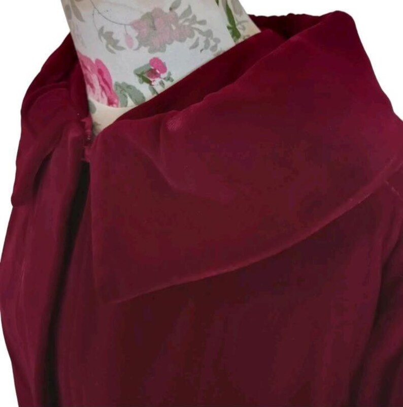 May include: A close-up of a burgundy-colored garment with a wide, draped collar. The fabric appears to be soft and flowing, with a slight sheen. The collar is the focal point, creating a dramatic effect. The garment is displayed on a mannequin.