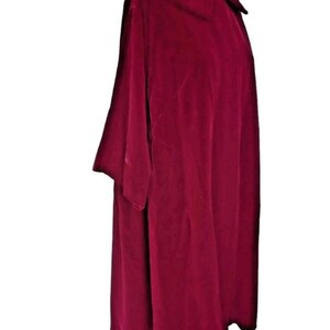 May include: A deep burgundy velvet cape with a wide collar and short sleeves. The cape is draped over a wooden mannequin, showcasing its flowing design. The fabric has a soft, luxurious texture, and the color is rich and vibrant.