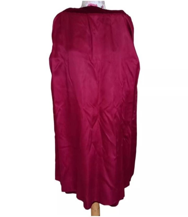 May include: A long, flowing cape in a deep burgundy color. The cape is made of a smooth, shiny fabric and has a scalloped hemline. The cape is displayed on a mannequin.