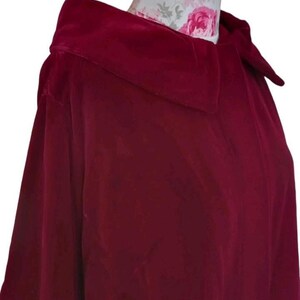 May include: A deep burgundy velvet cape with a wide collar. The cape is made of a soft, luxurious fabric and drapes elegantly. The collar is structured and adds a touch of sophistication to the garment. The cape is a rich, solid color.