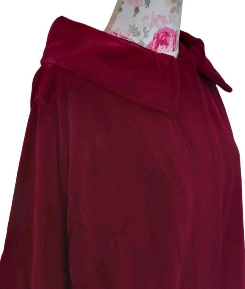 May include: A deep burgundy velvet cape with a wide collar. The cape is made of a soft, luxurious fabric and drapes elegantly. The collar is structured and adds a touch of sophistication to the garment. The cape is a rich, solid color.