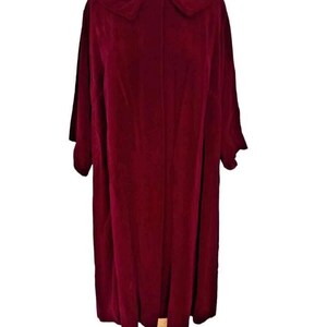 May include: A burgundy velvet coat with a large collar and short sleeves. The coat is displayed on a wooden dress form. The fabric has a soft, luxurious appearance, and the coat appears to be knee-length.