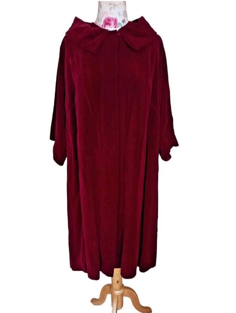 May include: A burgundy velvet coat with a large collar and short sleeves. The coat is displayed on a wooden dress form. The fabric has a soft, luxurious appearance, and the coat appears to be knee-length.