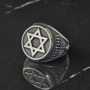 May include: A silver ring with a detailed Star of David design on the front and a menorah design on the band.