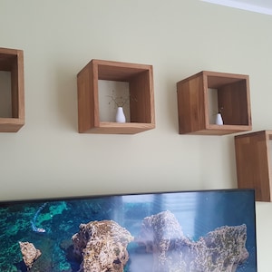 Può includere: Quattro mensole quadrate in legno montate su una parete, ciascuna con un piccolo vaso bianco contenente fiori secchi.