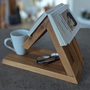 May include: Wooden book stand with a white mug and glasses on a shelf. The book stand is shaped like a house and has a book titled "H.G. Wells - The Time Machine" on top.