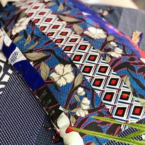 Op de afbeelding: Een assortiment stoffen sjaals met patronen in verschillende ontwerpen. De sjaals hebben bloemen-, geometrische en abstracte patronen in blauw, rood, wit en zwart. Sommige sjaals hebben de tekst "ARTING COLOUR OF CHINA".