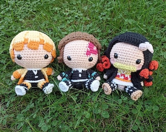 Op de afbeelding: Drie gebreide anime-personages met verschillende haarkleuren en kleding. De personages zitten op een bed van groen gras.