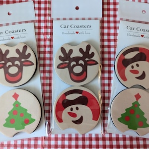 May include: Set of six car coasters featuring a Christmas theme. The coasters are round and have a white background with red, brown, and green accents. The designs include a snowman, a reindeer, and a Christmas tree.