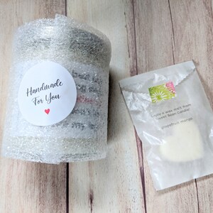 Puede incluir: Un tarro de vela blanco envuelto en pl&aacute;stico de burbujas con una pegatina que dice "Handmade for You" con un coraz&oacute;n rojo. Una fusi&oacute;n de cera blanca en una bolsa de papel blanca con el texto "Enjoy a wax melt from Sweet Bean Candle! grapefruit mango".
