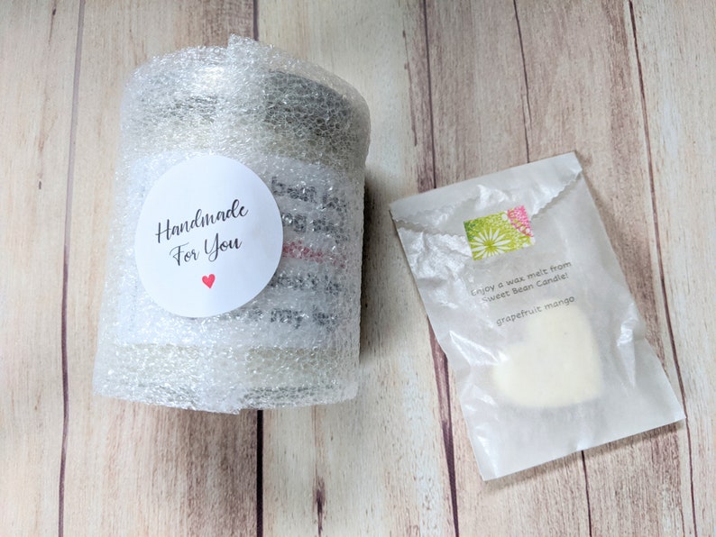 Puede incluir: Un tarro de vela blanco envuelto en pl&aacute;stico de burbujas con una pegatina que dice "Handmade for You" con un coraz&oacute;n rojo. Una fusi&oacute;n de cera blanca en una bolsa de papel blanca con el texto "Enjoy a wax melt from Sweet Bean Candle! grapefruit mango".