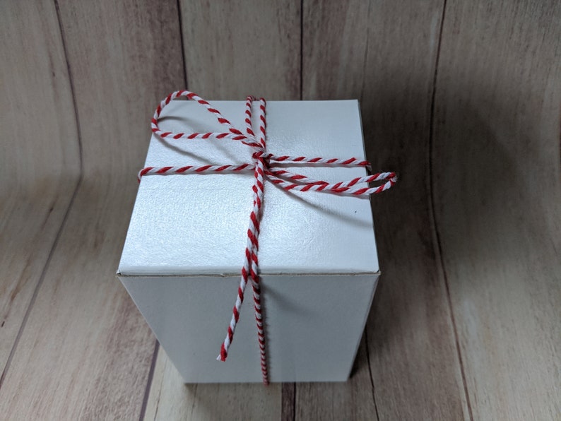 Puede incluir: Una caja de regalo blanca atada con cuerda de panadero roja y blanca.