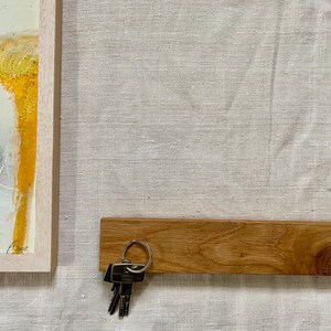 Pu&ograve; includere: Un porta chiavi in legno con un set di chiavi appese. Il porta chiavi &egrave; montato su una parete di colore beige chiaro.