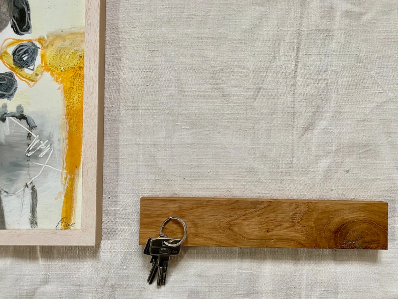 Pu&ograve; includere: Un porta chiavi in legno con un set di chiavi appese. Il porta chiavi &egrave; montato su una parete di colore beige chiaro.